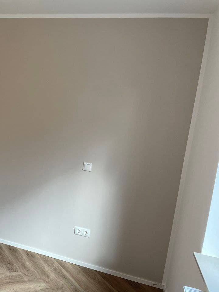 Wandfläche in warmem Greige, die an einer geraden senkrechten Kante auf die weiße Nachbarwand trifft