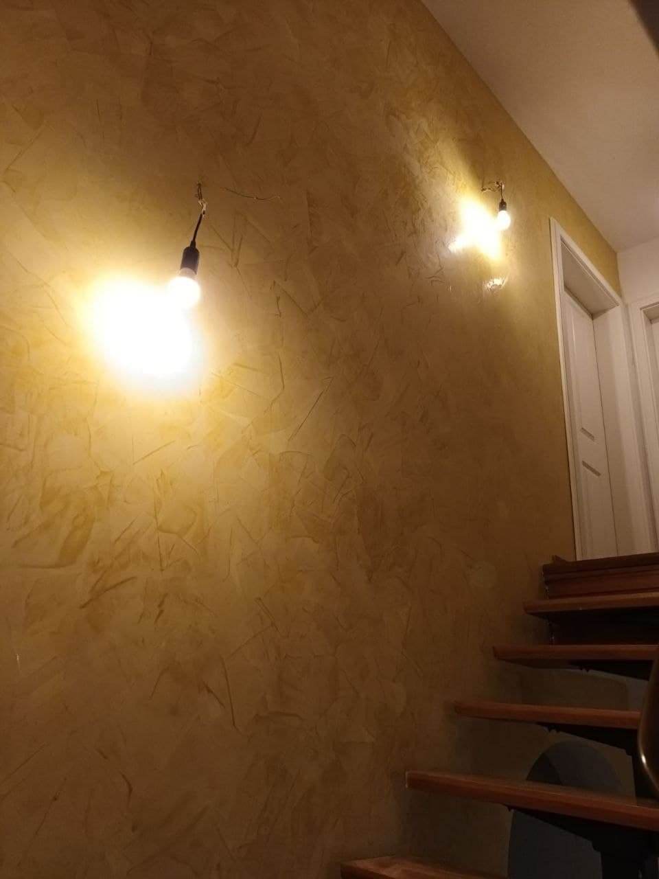 Treppenhaus mit warm goldener, strukturierter Wandfläche und zwei einfachen Wandleuchten