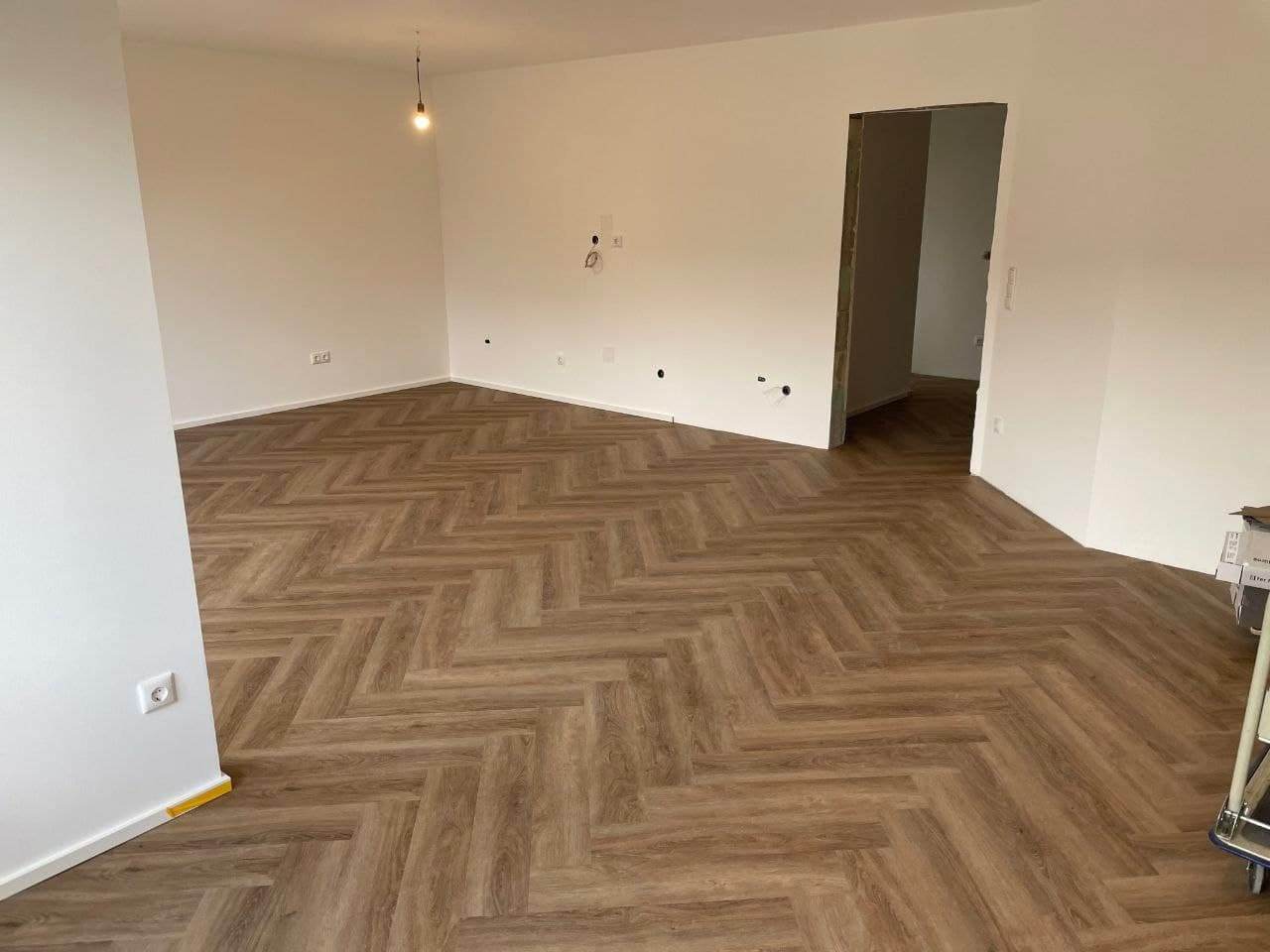 Leerer Wohnraum mit fertigen hellen Wandflächen, weißer Decke und Fischgrätboden