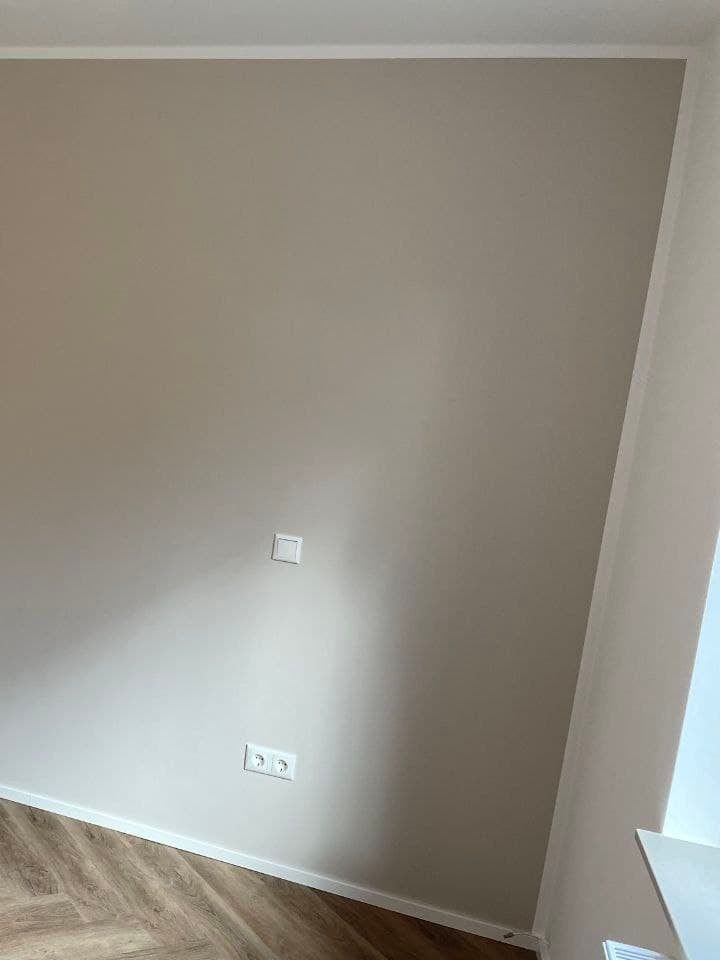 Wandfläche in warmem Greige, die an einer geraden senkrechten Kante auf die weiße Nachbarwand trifft