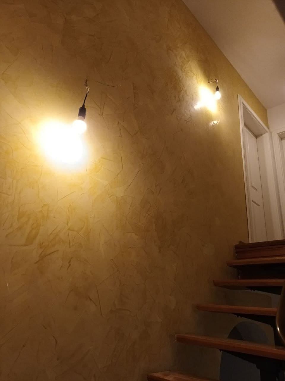 Treppenhaus mit warm goldener, strukturierter Wandfläche und zwei einfachen Wandleuchten
