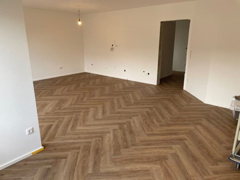 Leerer Wohnraum mit fertigen hellen Wandflächen, weißer Decke und Fischgrätboden